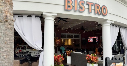 Exterior view of a bistro with outdoor seating, string lights, and a vintage car visible through the entrance.