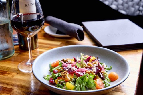 A fresh salad with mixed greens, colorful vegetables, and nuts, paired with a glass of red wine on a wooden table.