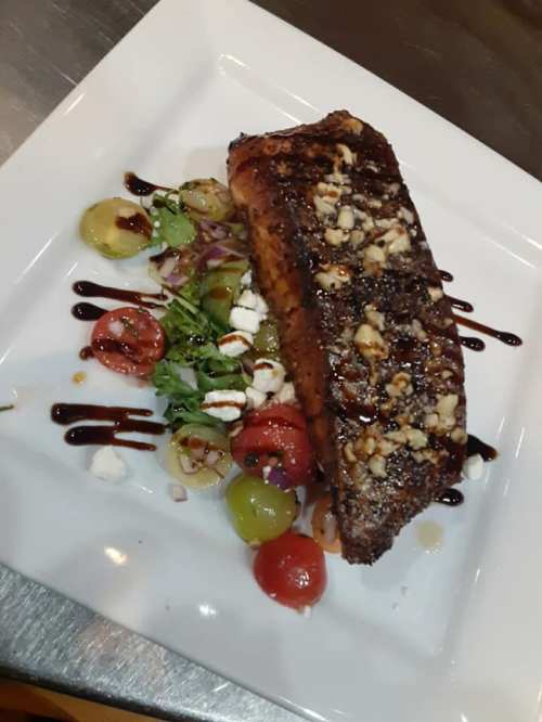 A beautifully plated salmon fillet topped with nuts, served with a fresh salad of mixed greens and cherry tomatoes.