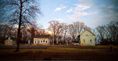 A serene landscape featuring two rustic houses and bare trees under a twilight sky with a hint of moonlight.