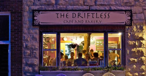 A cozy café and bakery named "The Driftless," with warm lighting and patrons visible through the window.
