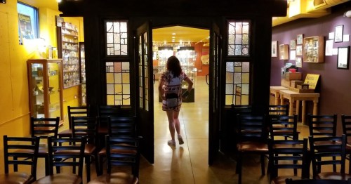 A person walks through a large doorway into a brightly lit room filled with shelves and chairs.