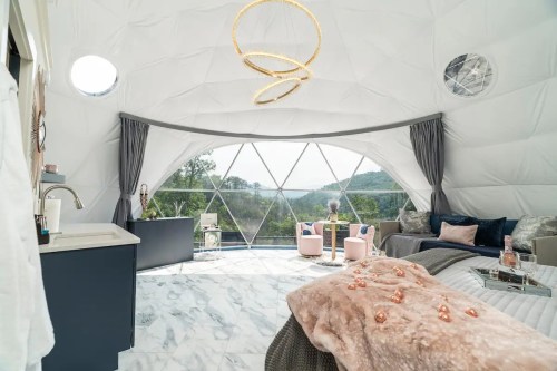 A modern, airy dome interior with large windows, plush seating, and scenic views of nature. Cozy and stylish decor.