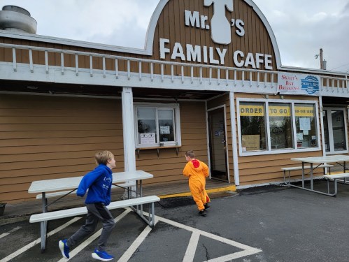 Two children play outside Mr. T's Family Cafe, one in a bright orange outfit and the other in a blue hoodie.