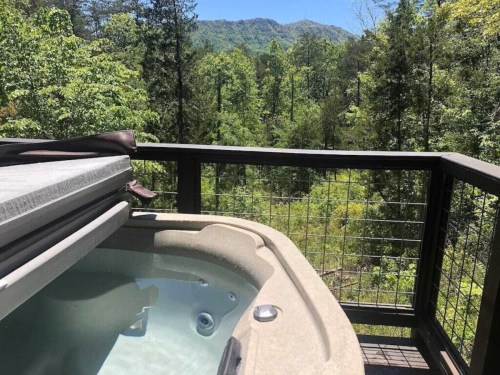 A hot tub on a deck overlooking a lush green forest and mountains in the background.