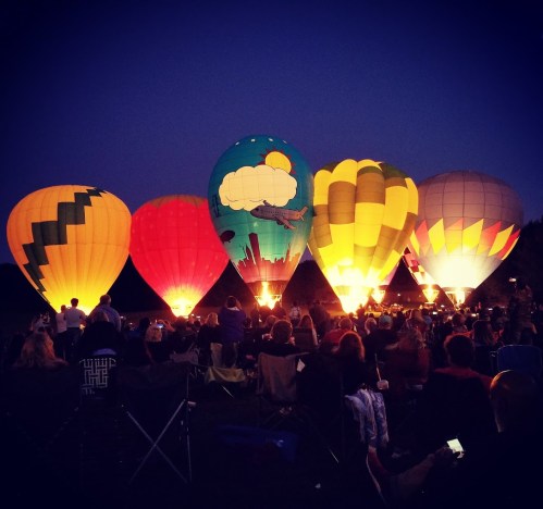 Colorful hot air balloons illuminated at night, with a crowd of spectators enjoying the vibrant display.