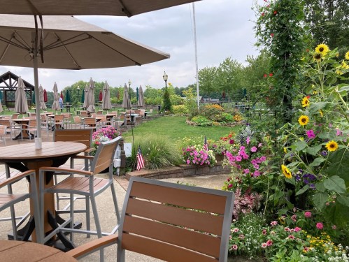 Outdoor dining area with tables, umbrellas, and vibrant flower beds in a lush garden setting.