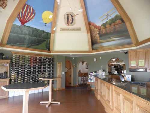 Interior of a winery with wooden decor, a curved ceiling featuring murals, and a wine display on the wall.