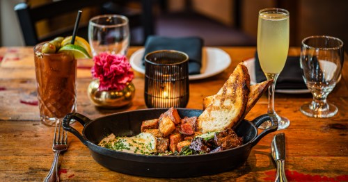 a rustic wood table with candlelight, cocktails, and a meal served in a cast iron pan