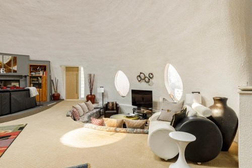 Modern living room with curved walls, unique windows, and cozy seating arrangements. Bright and inviting atmosphere.