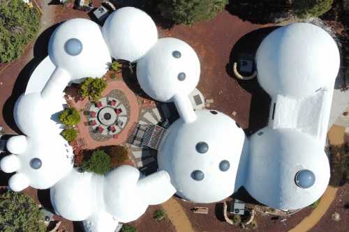 Aerial view of a unique, white, organic-shaped building complex surrounded by greenery and a circular patio.