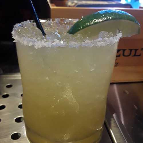 A refreshing margarita in a salt-rimmed glass, garnished with a lime wedge and a straw.