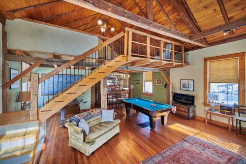Cozy living space with wooden beams, a pool table, and a staircase leading to a loft area. Warm, inviting atmosphere.