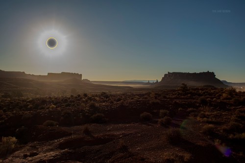 A stunning landscape at sunset featuring a solar eclipse over rocky formations and desert terrain.