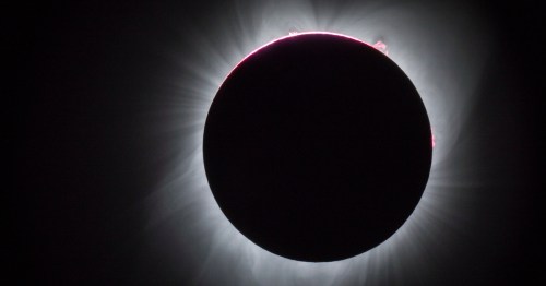 A solar eclipse with a darkened sun surrounded by a glowing corona and faint solar flares.