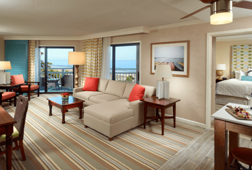 Bright hotel suite with a sofa, coffee table, and scenic ocean view through large windows. Cozy and inviting decor.