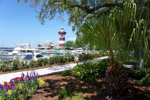 A vibrant marina scene featuring a striped lighthouse, boats, and lush greenery with colorful flowers in the foreground.