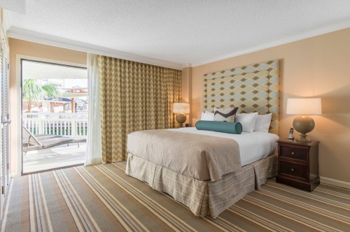 Cozy hotel room with a king bed, patterned headboard, and sliding door to a patio with outdoor seating.
