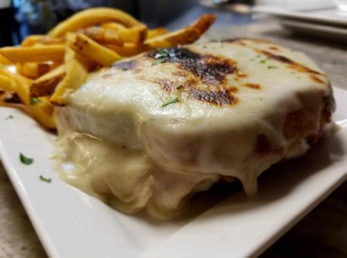 A melted cheese sandwich with crispy edges, served with a side of golden French fries on a white plate.