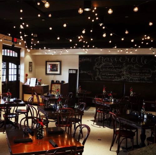 Cozy restaurant interior with string lights, wooden tables, and a chalkboard menu. Elegant and inviting atmosphere.