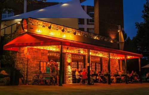 A cozy restaurant exterior illuminated at night, with people dining outside under warm lights.