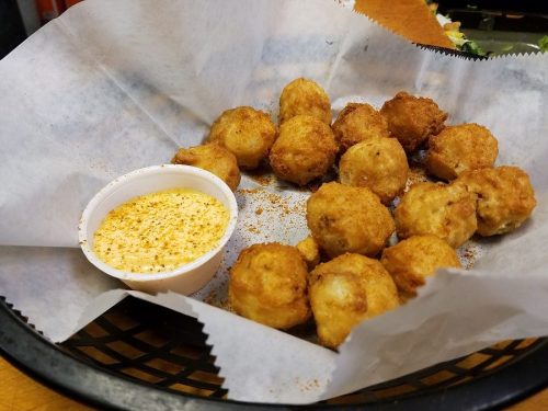 A basket of golden fried balls with a small cup of dipping sauce on the side, lined with parchment paper.