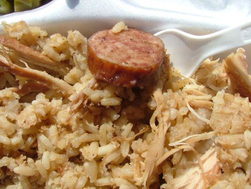 A close-up of a plate featuring rice, shredded chicken, and a slice of sausage, with a plastic fork beside it.