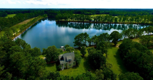 Aerial view of a serene lake surrounded by lush greenery and a charming house near the water's edge.