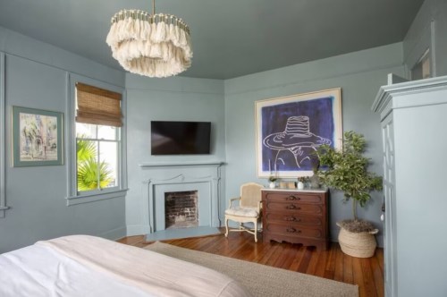 Cozy bedroom with blue walls, a chandelier, artwork, a TV, and wooden furniture, featuring a warm, inviting atmosphere.
