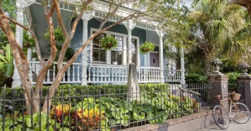 A charming blue house with a porch, surrounded by greenery and a bicycle parked nearby.
