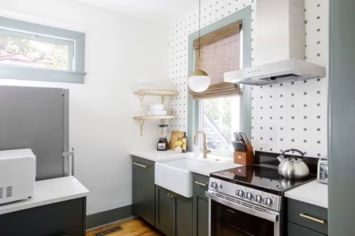 A modern kitchen featuring a farmhouse sink, dark cabinetry, and patterned wallpaper, with a stove and microwave.