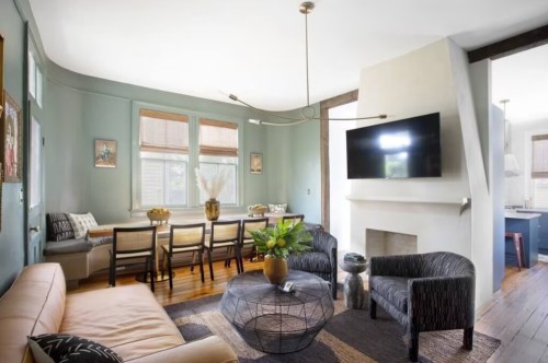A modern living room with a beige sofa, black chairs, a round coffee table, and a TV above a fireplace.