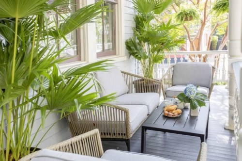 Cozy porch with comfortable seating, a coffee table, and lush green plants, creating a relaxing outdoor space.