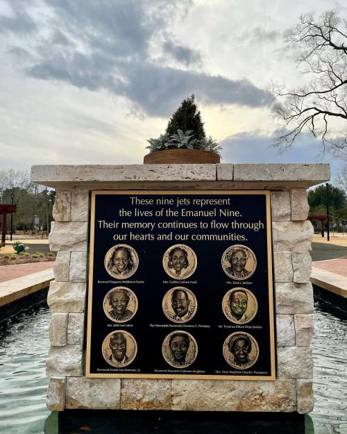A memorial plaque honoring the Emanuel Nine, featuring their names and portraits, set in a stone fountain.