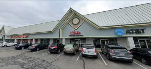 Exterior view of a shopping plaza featuring a restaurant, brewery, and AT&T store, with parked cars in front.