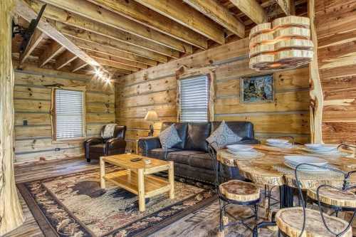 Cozy cabin interior with wooden walls, a leather sofa, a rustic dining table, and warm lighting.