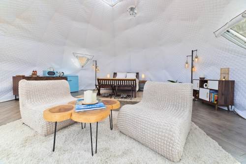 Cozy interior of a geodesic dome with two chairs, a wooden table, and a dining area, all in a bright, minimalist style.