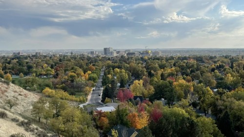 A panoramic view of a city skyline surrounded by colorful autumn trees under a partly cloudy sky.