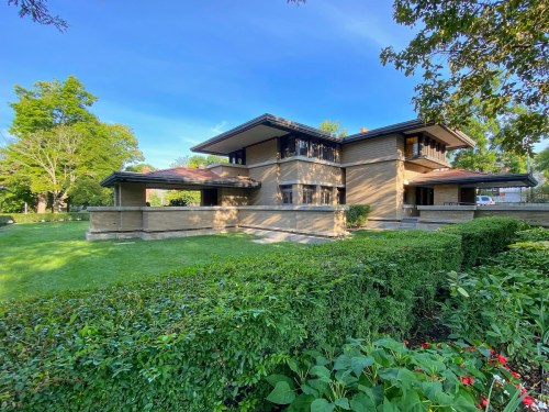 A modern two-story house with a flat roof, surrounded by lush greenery and a well-maintained lawn.