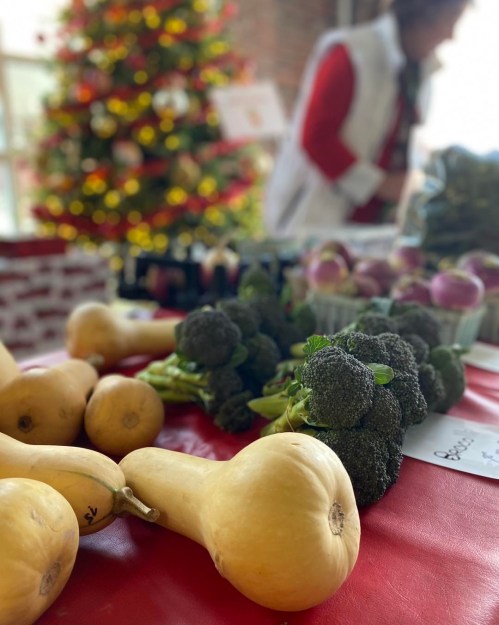 A table with fresh vegetables, including butternut squash and broccoli, with a decorated Christmas tree in the background.