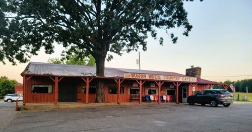 A rustic country cafe with a large tree in front, featuring a wooden exterior and outdoor seating.