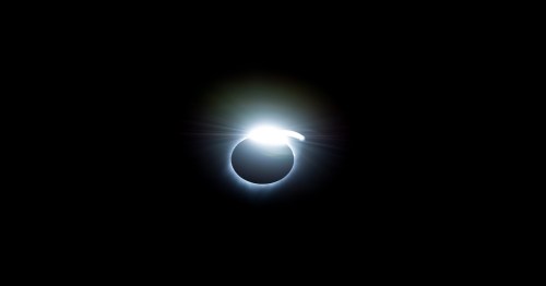 A bright light encircles a dark sphere, resembling a solar eclipse against a black background.