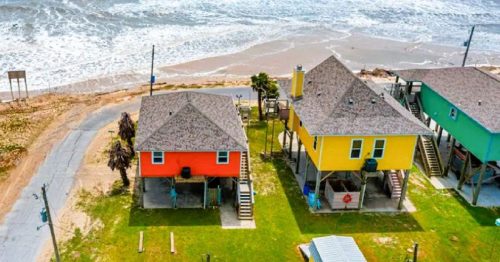 Aerial views of a colorful waterfront Airbnb in Holly Beach Louisiana with the sandy beach and crashing waves in the background.