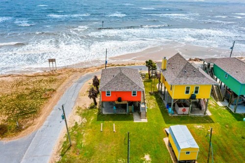 Aerial views of a colorful waterfront Airbnb in Holly Beach Louisiana with the sandy beach and crashing waves in the background