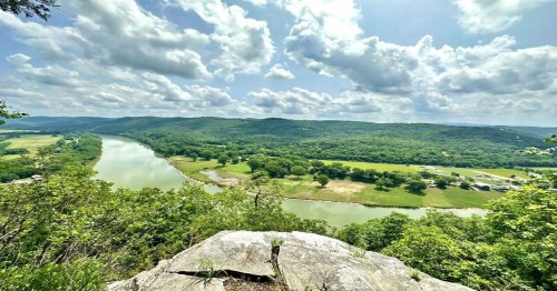 A panoramic view of a river winding through lush green hills under a partly cloudy sky.