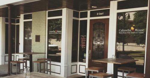 Exterior of Cahawba House, featuring a welcoming entrance and outdoor seating with wooden tables.