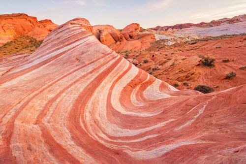 Colorful, wavy rock formations with red and white stripes under a clear sky, showcasing natural geological patterns.