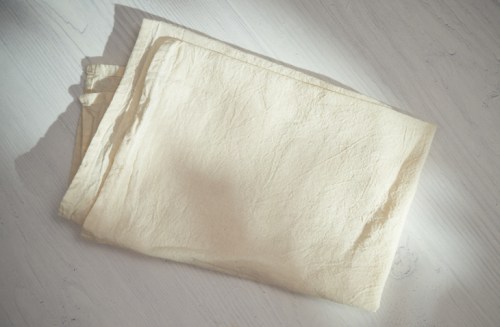 A neatly folded, light-colored fabric resting on a wooden surface, softly illuminated by natural light.