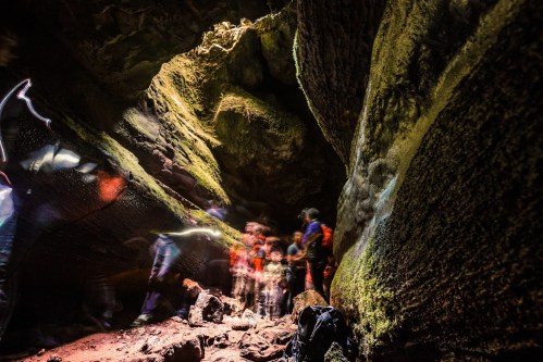 A group of people exploring a dark cave with moss-covered walls and a bright opening above.