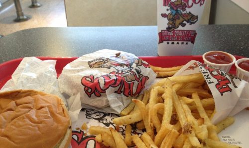 A tray with a burger, fries, and two cups of ketchup, alongside a takeout bag from a fast food restaurant.